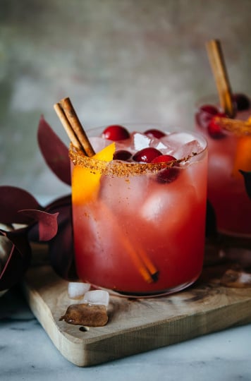 a head on shot of spiced cranberry orange margaritas garnished with cinnamon sticks and orange peels
