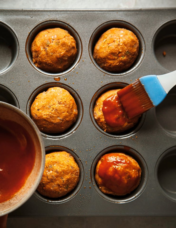 An overhead shot of vegan meatloaves being brushed with a ketchup and hot sauce mixture.