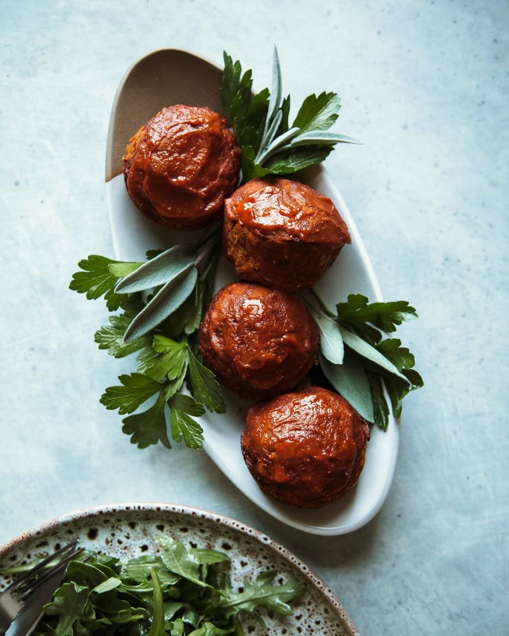 An overhead shot of a small oval platter that has 4 spicy buffalo meatloaf minis perched on top with sprigs of parsley and sage for garnish.