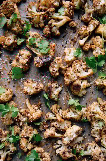 Overhead shot of maple tahini-glazed cauliflower on a sheet pan. Cauliflower is garnished with cilantro and sesame seeds.