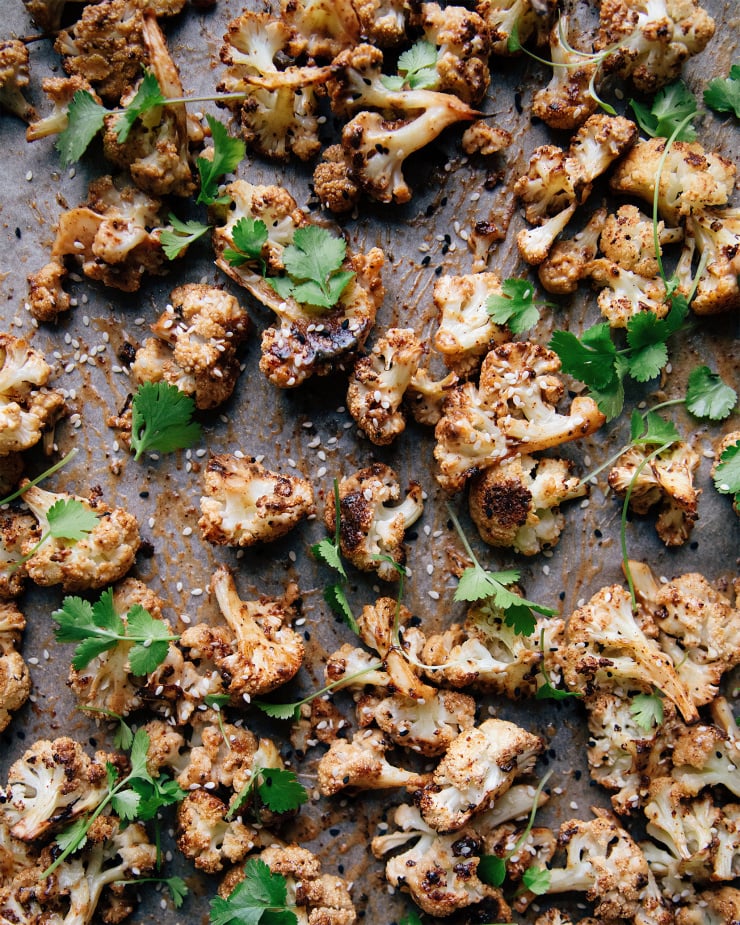 Overhead shot of maple tahini glazed cauliflower on a sheet pan. Cauliflower is garnished with cilantro and sesame seeds.