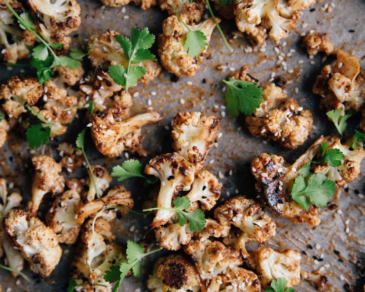 Overhead shot of maple tahini glazed cauliflower on a sheet pan. Cauliflower is garnished with cilantro and sesame seeds.
