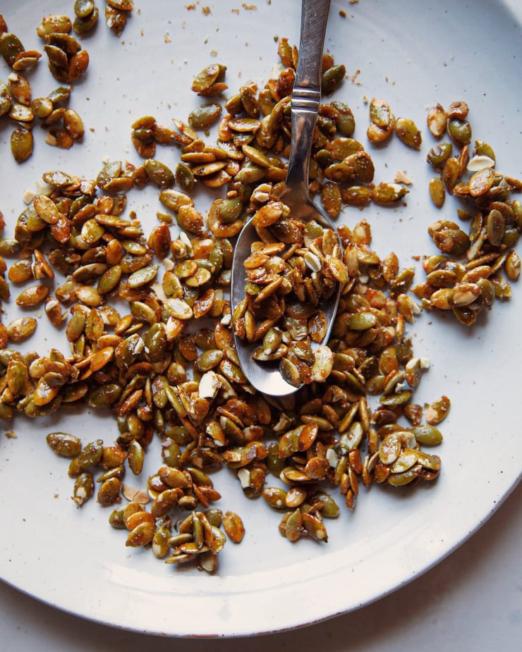 An up close shot of candied pumpkin seeds on a pale blue-white plate with a spoon.