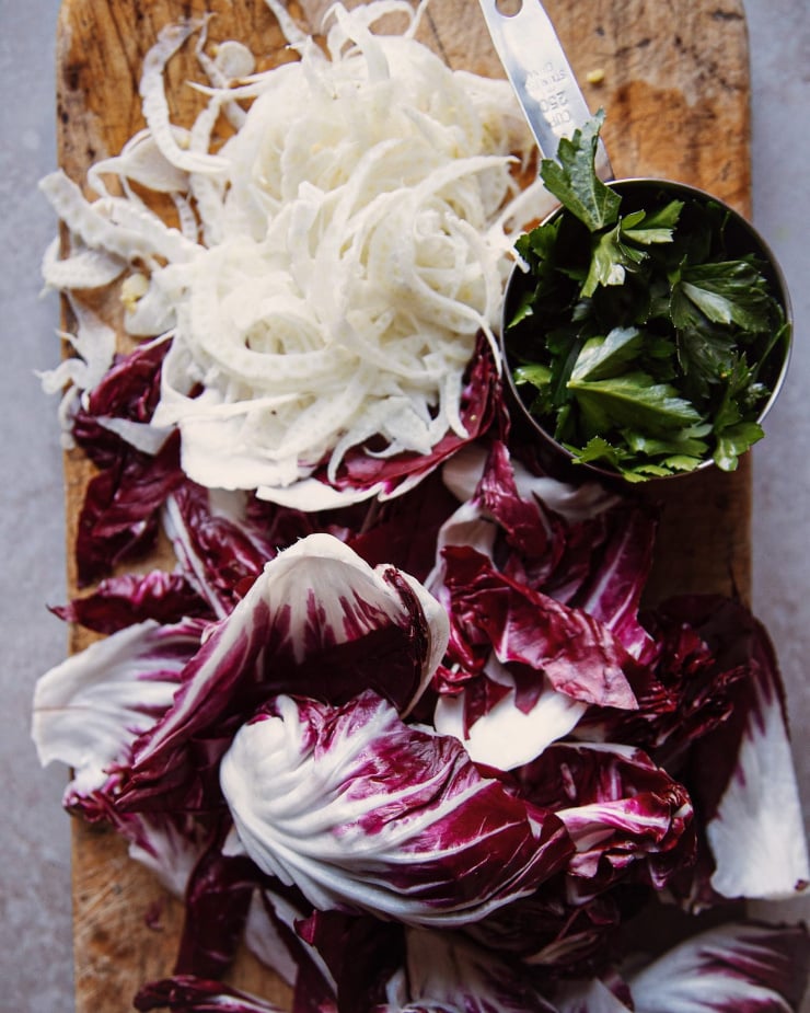 Torn radicchio, shaved fennel and a cup of parsley leaves on a wood chopping board.