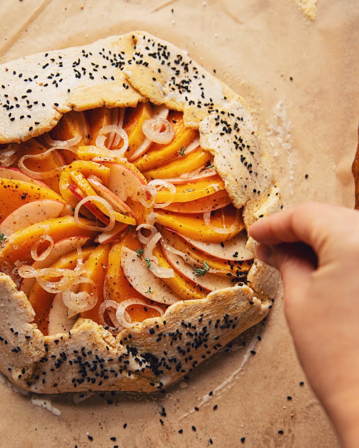 Overhead shot of a hand sprinkling nigella seeds on a galette, before baking.