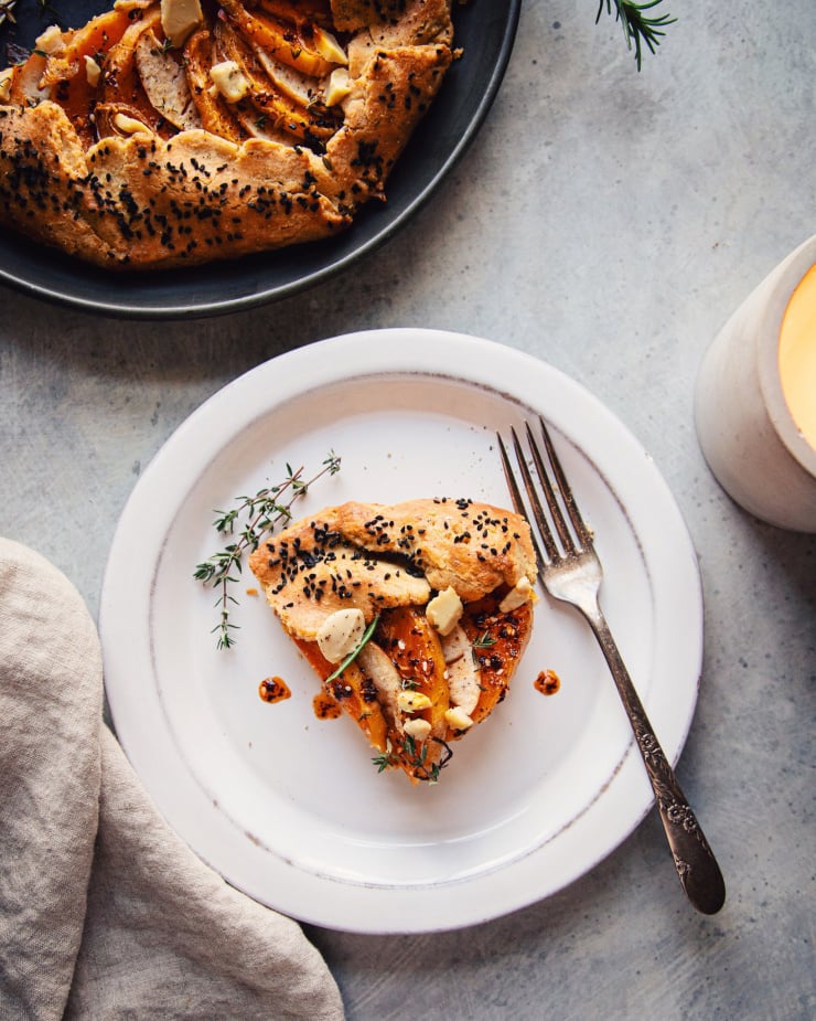 An overhead shot of a slice of vegan butternut galette on a weathered white plate on a mottled grey background.