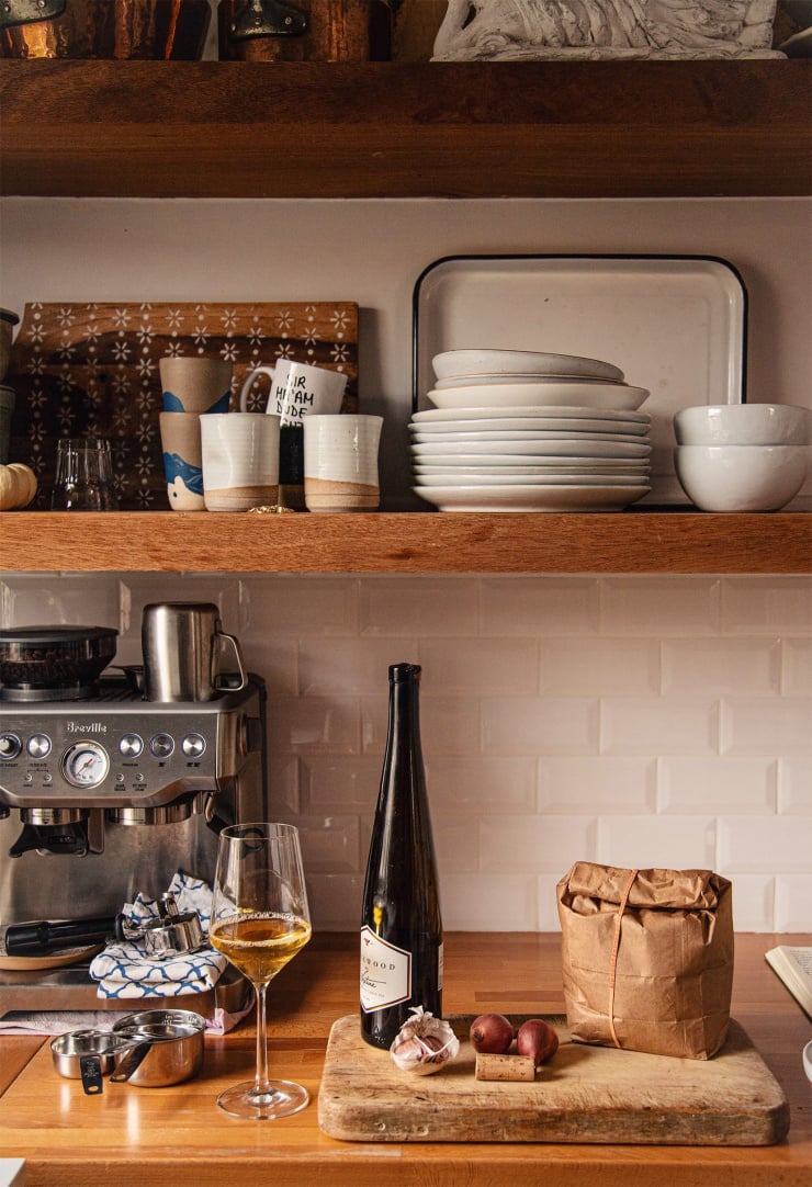 A shot of Laura's open kitchen shelving with a bottle of wine, a glass of wine, and a paper bag on the counter.