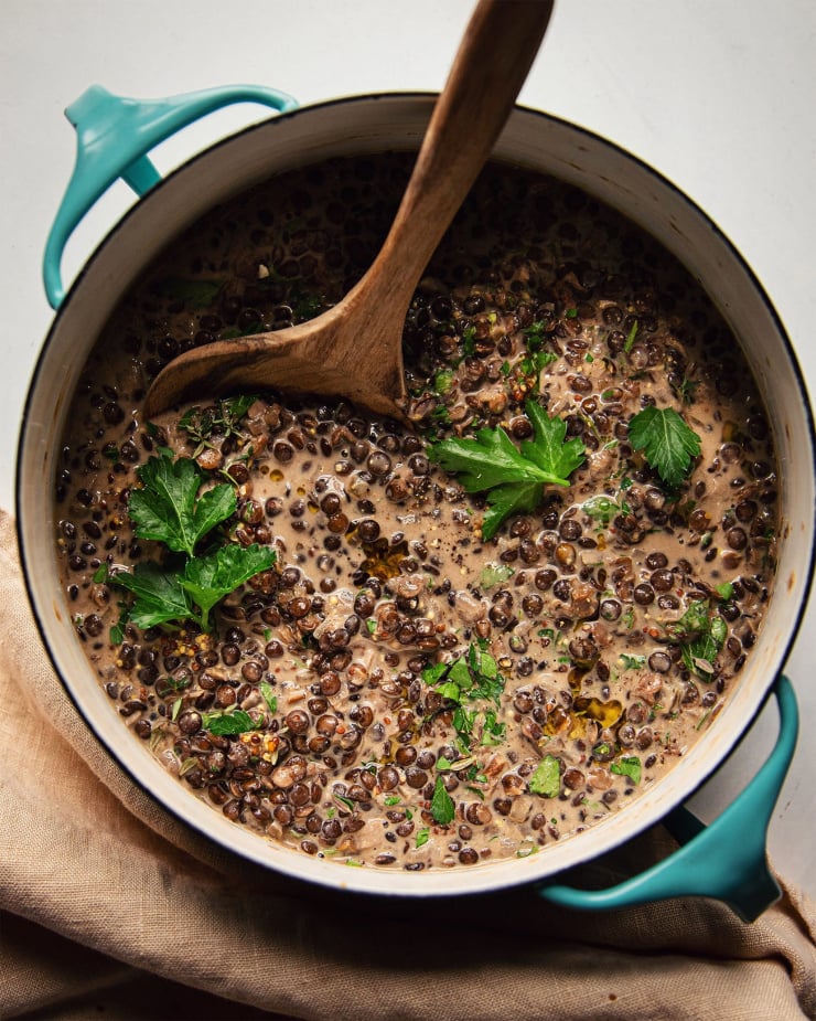 An overhead shot of white wine lentils in a turquoise pot, garnished with parsley