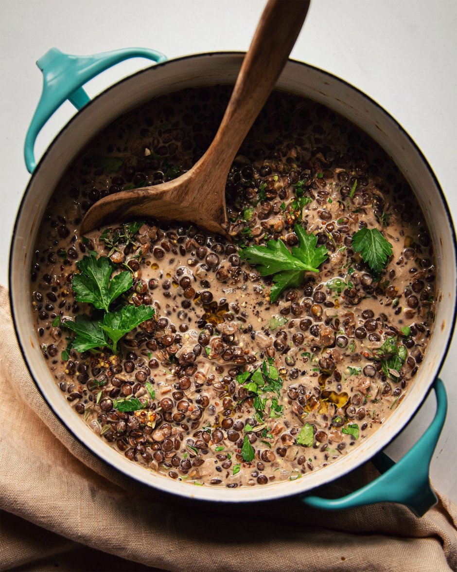 An overhead shot of white wine lentils in a turquoise pot, garnished with parsley
