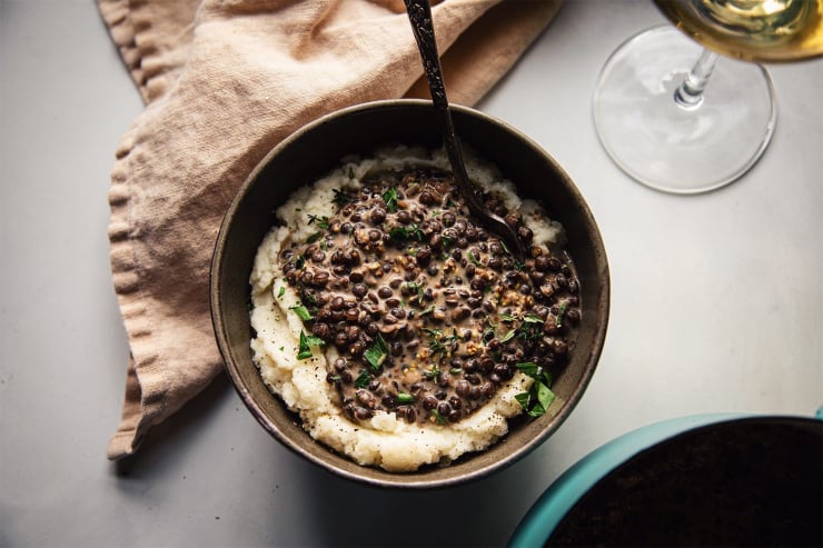 An overhead shot of a single serving of white wine lentils ladled on top of some creamy mashed cauliflower.