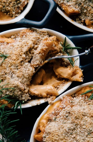 Vegan creamy red pepper pasta baked in small oblong black ramekins with crushed cracker topping.