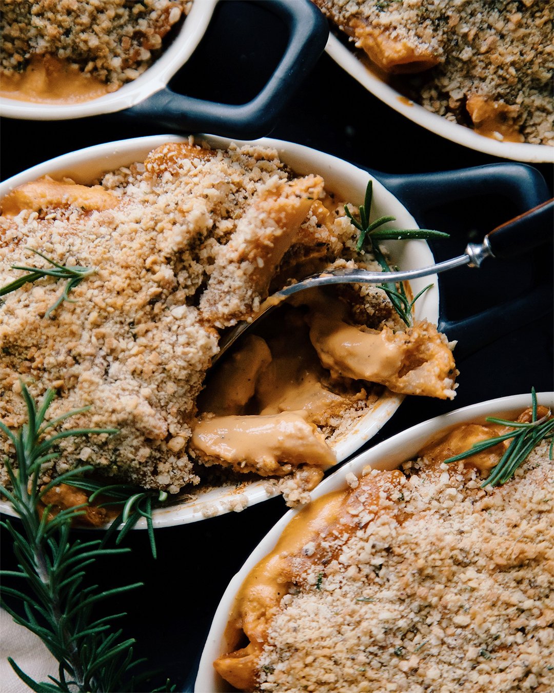 Vegan creamy red pepper pasta baked in small oblong black ramekins with crushed cracker topping.