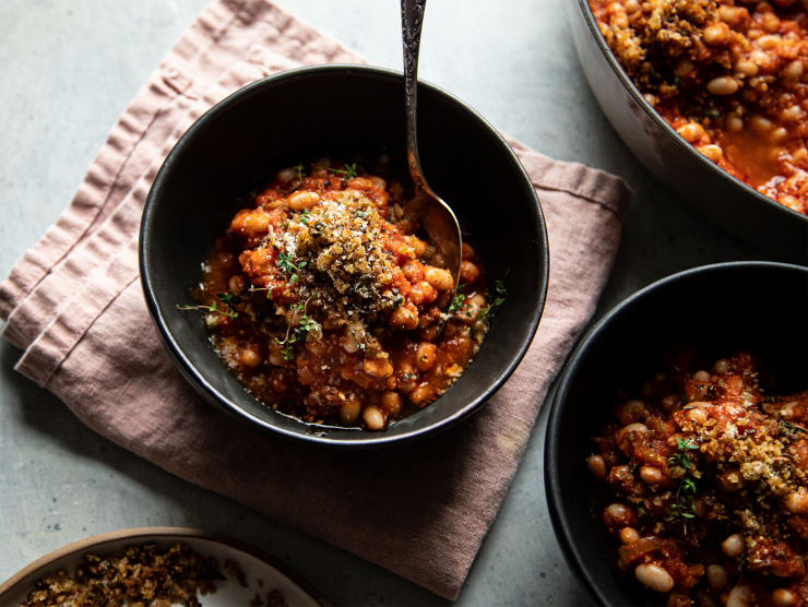 Overhead shot of a single serving of jammy sun dried tomato white beans. The white beans are plated in a matte back bowl on top of a pink napkin.
