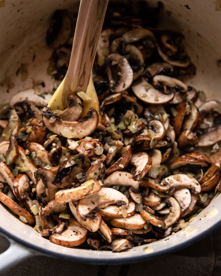 An up close, overhead shot of mushrooms being sauteed in a white Dutch oven pot.