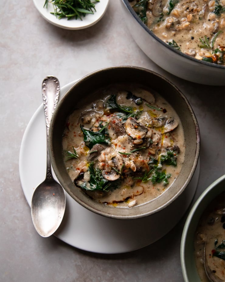 Overhead shot of a creamy vegan mushroom stew in a deep, olive green bowl, set on a white plate, on top of a grey stone background.