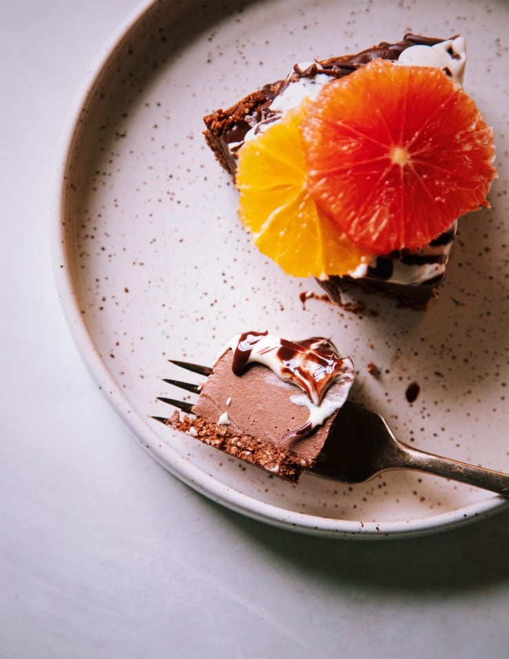 An up close, overhead shot of a slice of chocolate cheesecake with a forkful nearby on a white speckled plate.