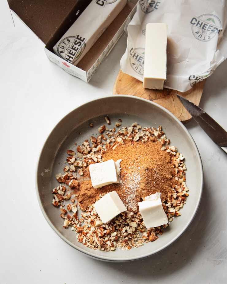 An overhead shot of pecan streusel being made in a grey bowl. In the bowl, there is: chopped pecans, coconut sugar, and 3 big cubes of vegan butter.