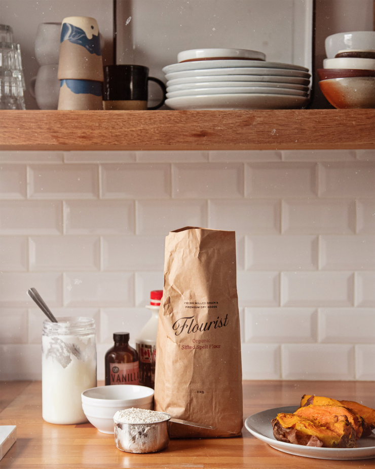 A head on shot of muffin ingredients on a wood butcher block counter with open shelving and white subway tile in the background.