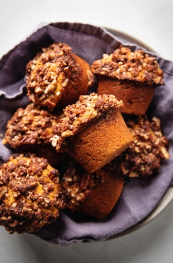 An overhead shot of vegan sweet potato muffins perched inside of a bowl that is lined with a navy blue linen napkin.