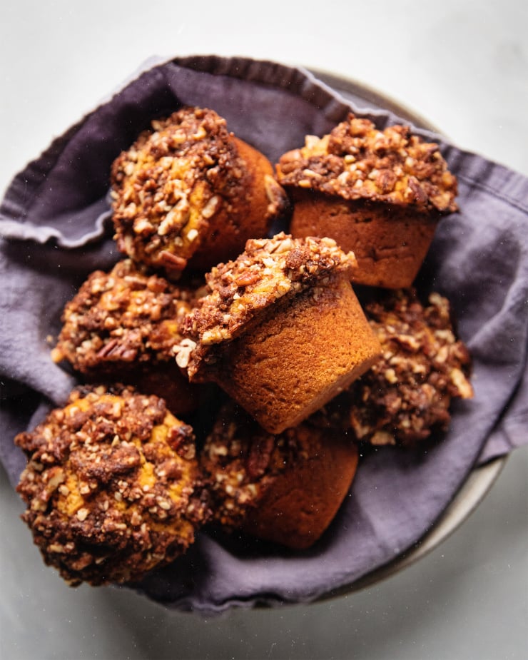 An overhead shot of vegan sweet potato muffins perched inside of a bowl that is lined with a navy blue linen napkin.