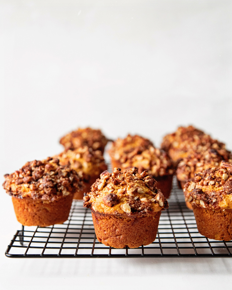 A head on shot of vegan sweet potato muffins with pecan streusel, sitting on top of a black cooling rack with a white background.