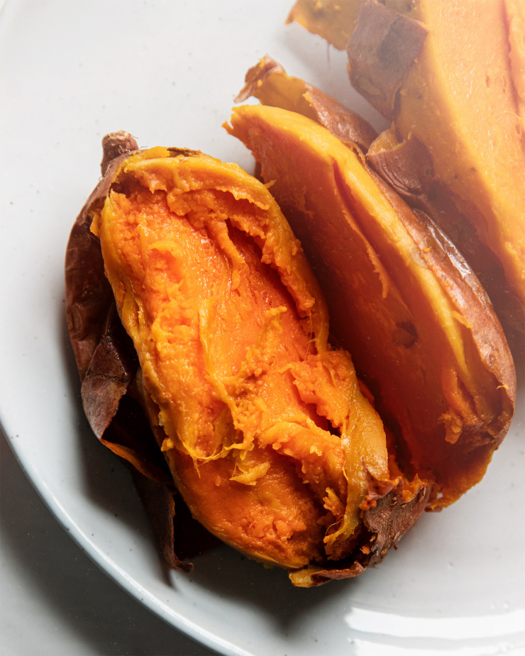 An up close, overhead shot of a split open baked sweet potato on a white plate.
