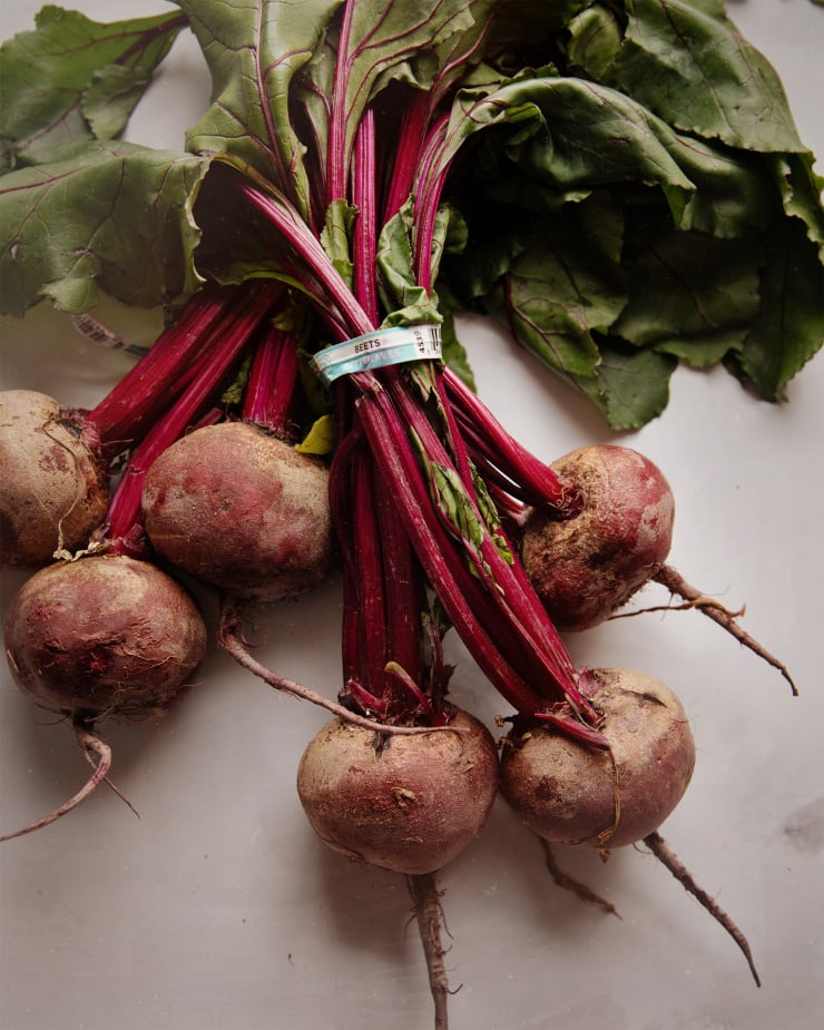 An overhead shot of two bunches of beets with greens on a white background. The lighting is soft and natural.