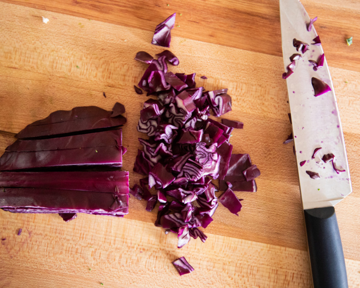 Image shows red cabbage being chopped on a wood cutting board.