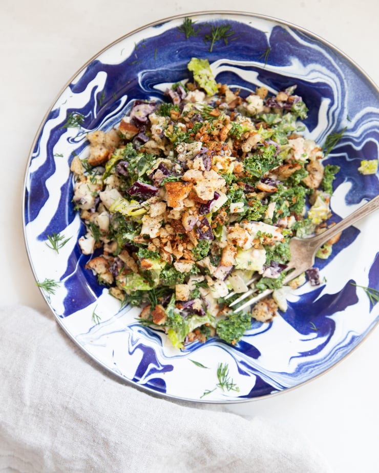 An overhead shot of a colourful chopped dill pickle salad with creamy dressing on top of a blue, swirly patterned plate.