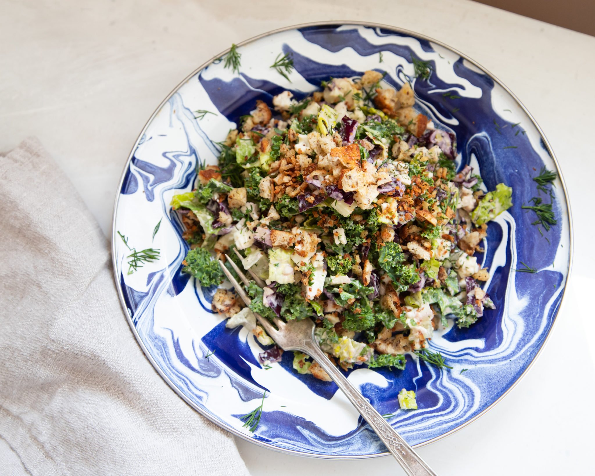 An overhead shot of a colourful chopped salad with creamy dressing on top of a blue, swirly patterned plate.