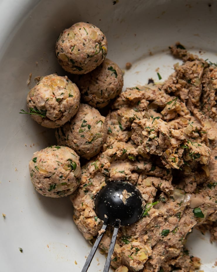 An overhead, up close shot of a savoury mixture being rolled into balls, pre cooking.