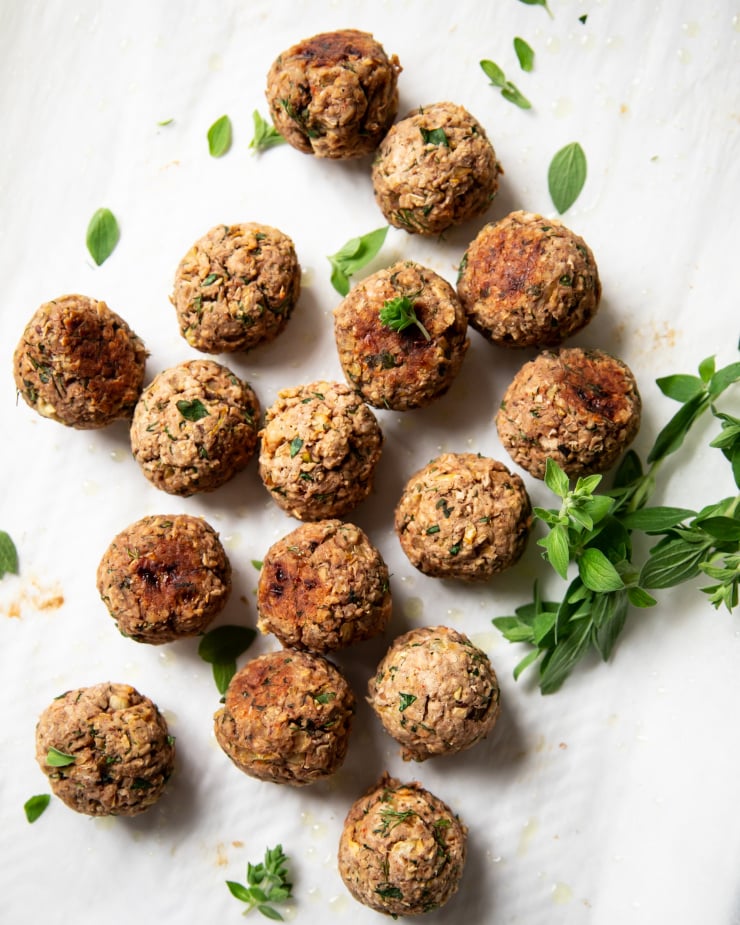 An overhead shot of cooked vegan meatballs, garnished with fresh oregano leaves.