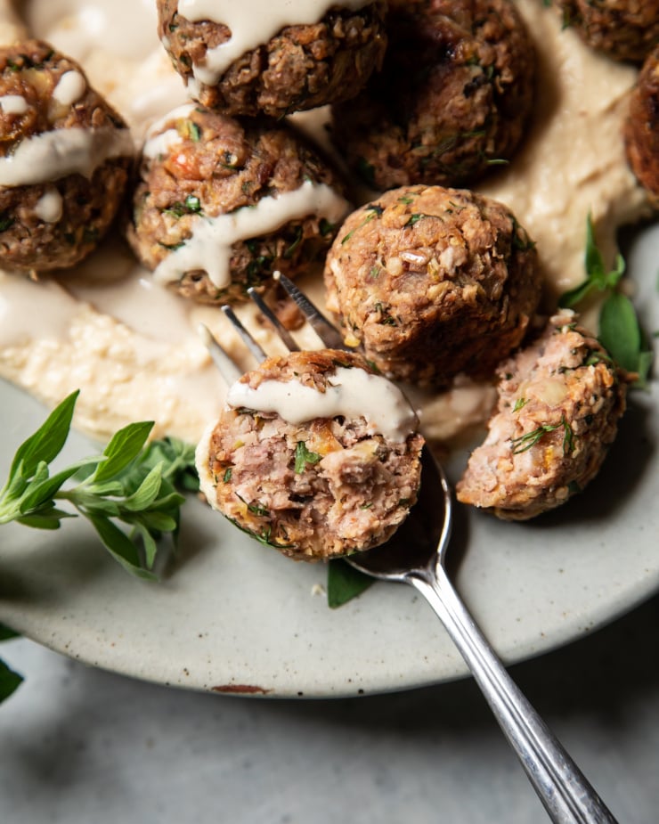 An overhead, up close shot of vegan meatballs, drizzled with tahini sauce and plated on top of hummus.