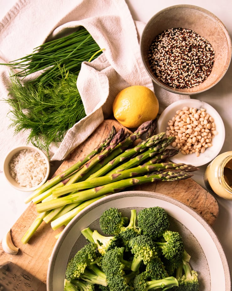 Overhead image shows ingredients for a green love quinoa salad on a worn wood and mottled white background.