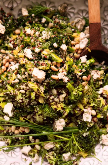 Image shows a green love quinoa salad in a patterned white bowl. The salad is garnished with whole blades of chives and bits of soft vegan cheese.