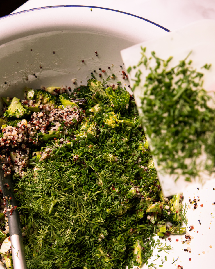 Image shows chopped dill and chives being added to a bowl of quinoa salad.