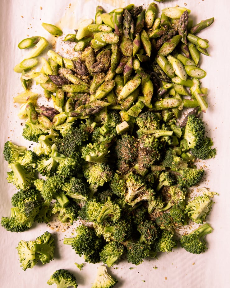 An overhead shot of small-diced broccoli and asparagus on a parchment lined baking sheet.