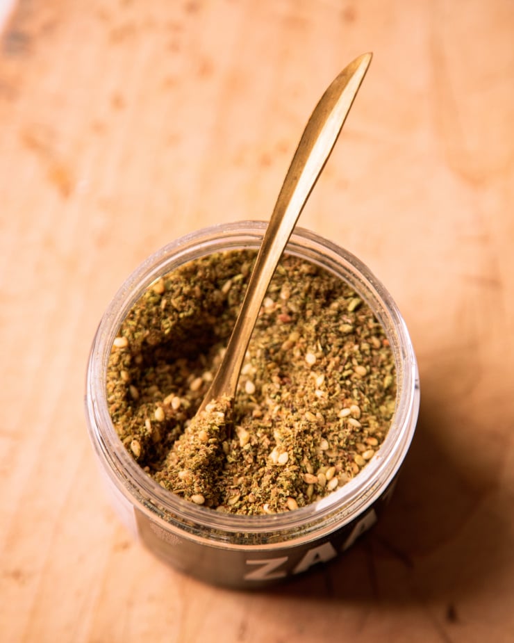 An up close shot of a jar of za'atar spice with a gold spoon sticking out.