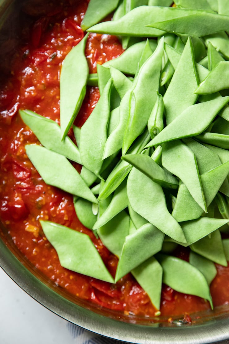 An up close, overhead image of cut Romano beans in a pan of tomato sauce.