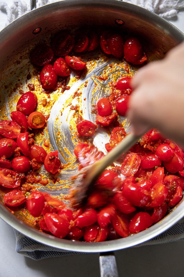An overhead shot of a hand stirring some cherry tomatoes in a sauté pan.