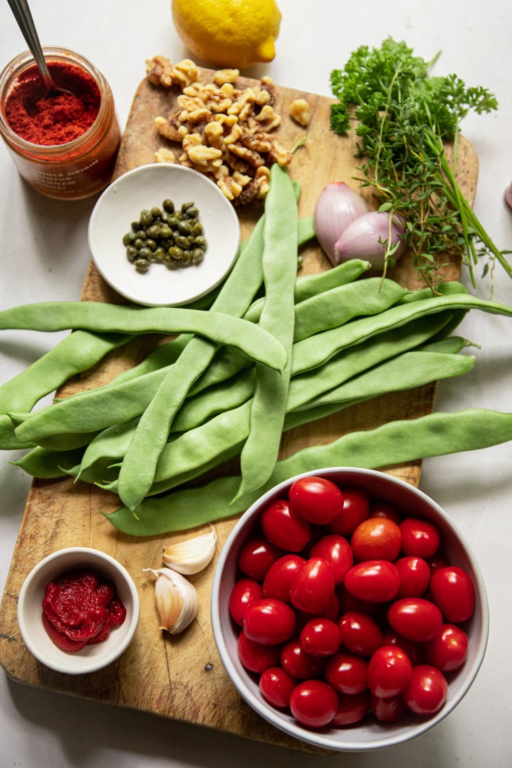 An overhead shot of ingredients for briased romano beans with spicy cherry tomato sauce. Ingredients are shown on a worn wooden board.