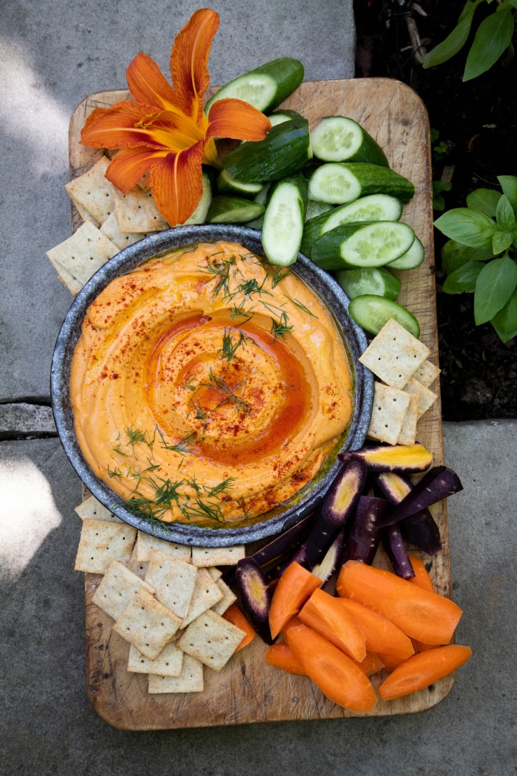An overhead shot of a creamy, light orange dip surrounded by crackers and cut vegetables. Part of a roundup of vegan appetizer recipes.
