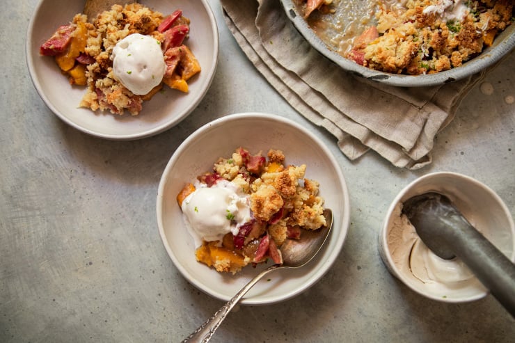 An overhead shot of a fruit crumble dessert in white serving bowls. Each serving is topped with a melt-y scoop of ice cream.