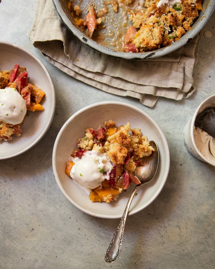 An overhead shot of a fruit crumble dessert in white serving bowls. Each serving is topped with a melt-y scoop of ice cream.