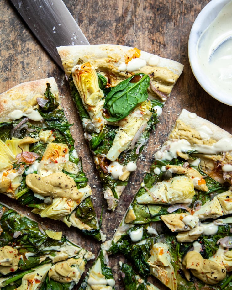Overhead: up close image of a sliced pizza. The blade of a knife is nearby. Pizza is shown on a worn wood background.