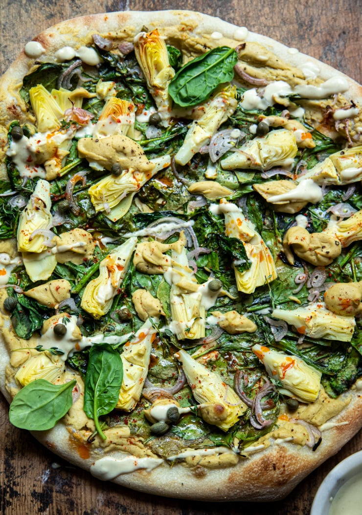 Overhead: up close image of a pizza with spinach and a creamy sauce. Pizza is shown on a worn wood background.