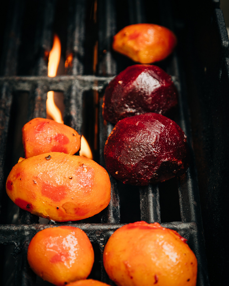 Image shows beet halves on a grill. A flame is kicking up in the background.