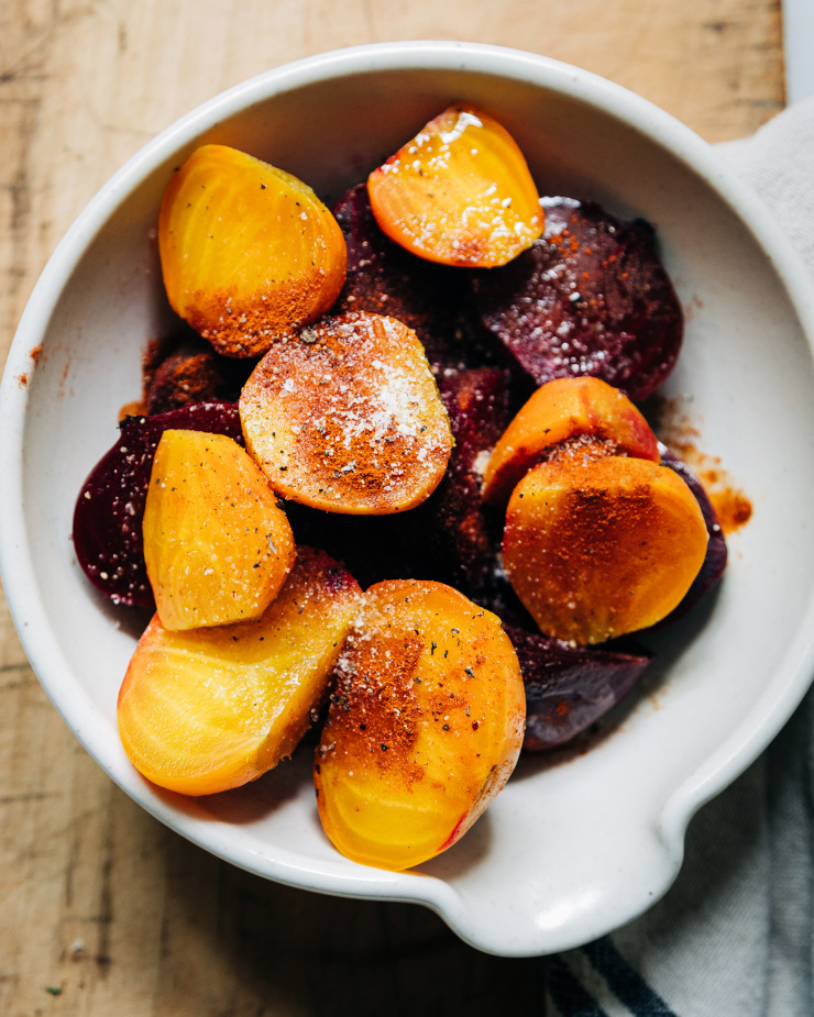 An overhead shot of cooked and diced beets in a white bowl. The beets have a sprinkle of spices on top.