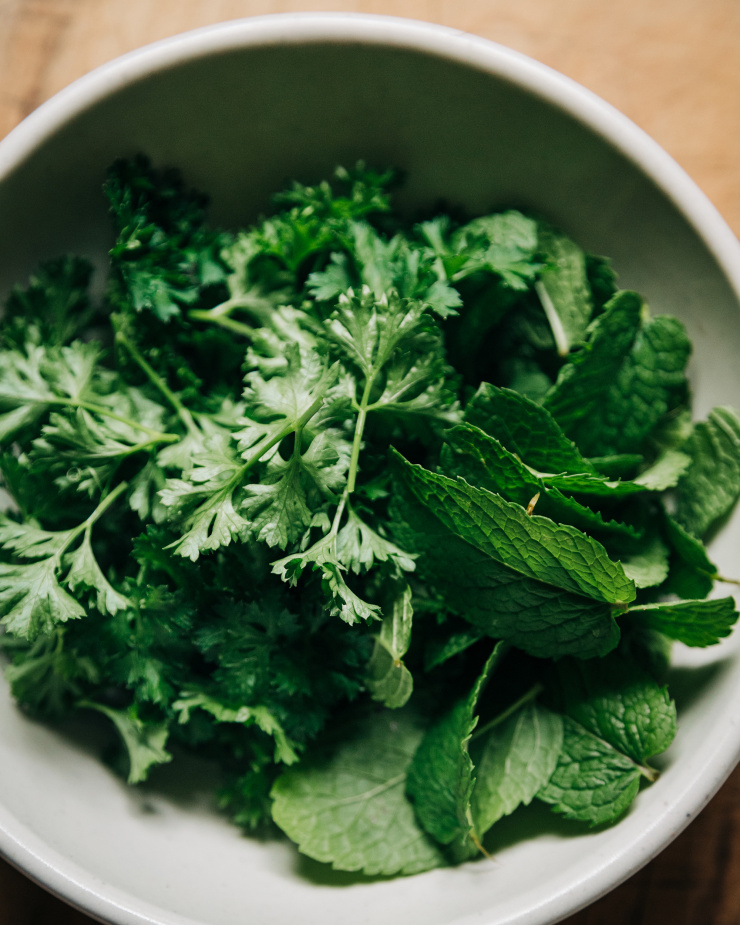 An up close, overhead shot of parsley and mint leaves in a white bowl.