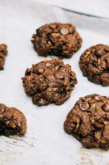 A 3/4 angle shot of chocolate zucchini muffin tops on a white parchment background.